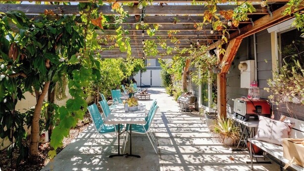 An outdoor patio with a pergola, seating area, and a grill.