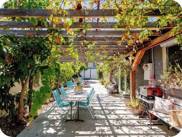 Un patio exterior con pérgola, zona de estar y una parrilla.