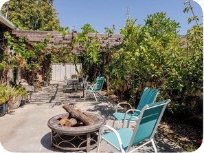 Un patio exterior con un hogar para fogata, sillas y plantas en macetas.