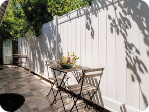 Un patio con una mesa, sillas, una planta en maceta y una valla blanca.