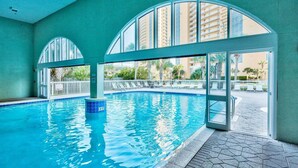 Una piscina interior con paredes de vidrio transparente, suelo de baldosas y vistas a una zona residencial.