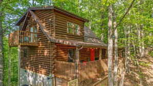 A log cabin with a balcony and a deck, surrounded by trees.