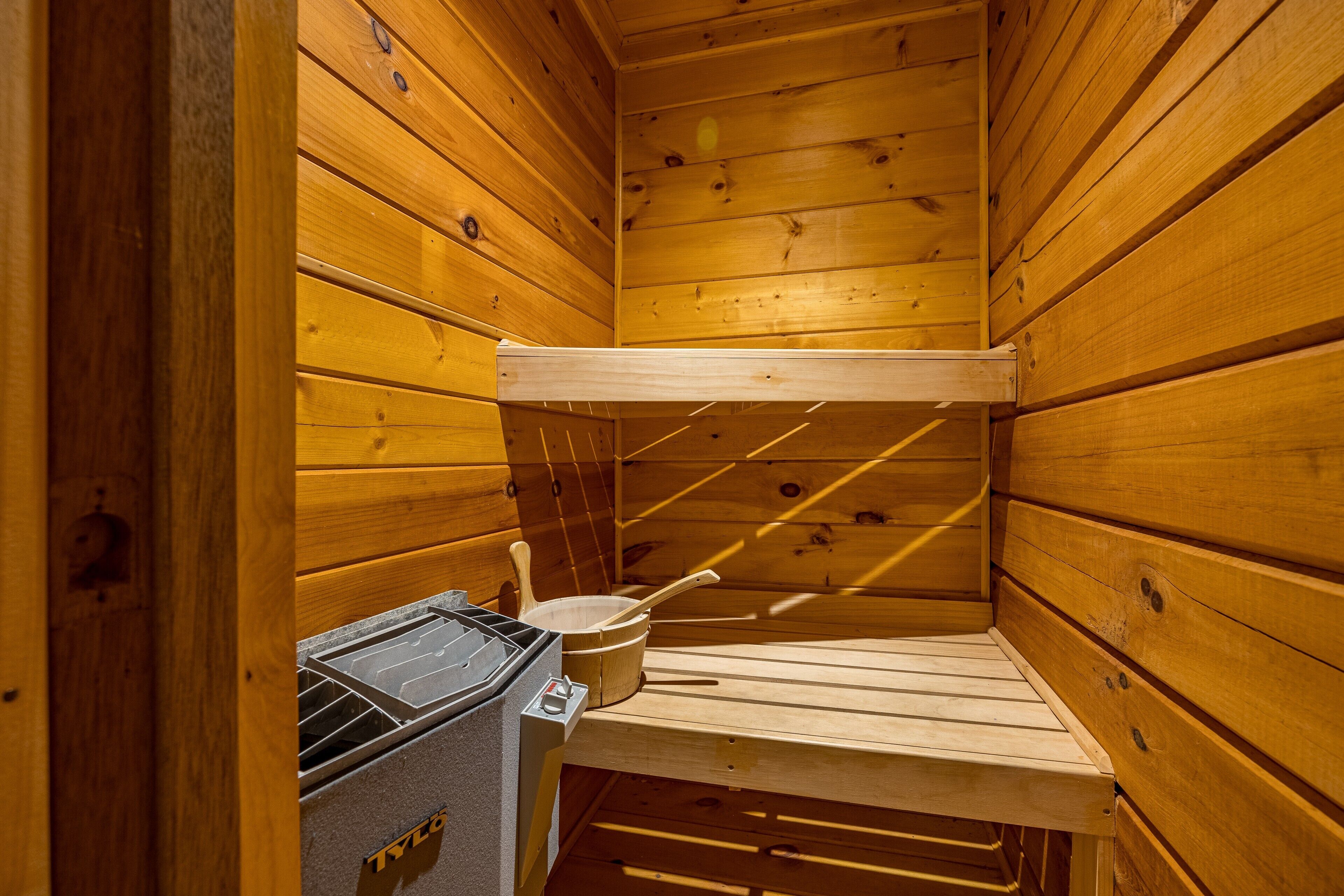 Eine Sauna mit Holzwänden, einer Sitzbank, einem Eimer und einer Heizung.