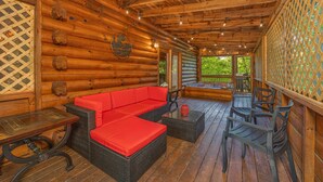 A log cabin interior with a red sofa, wicker furniture, and a wooden deck.