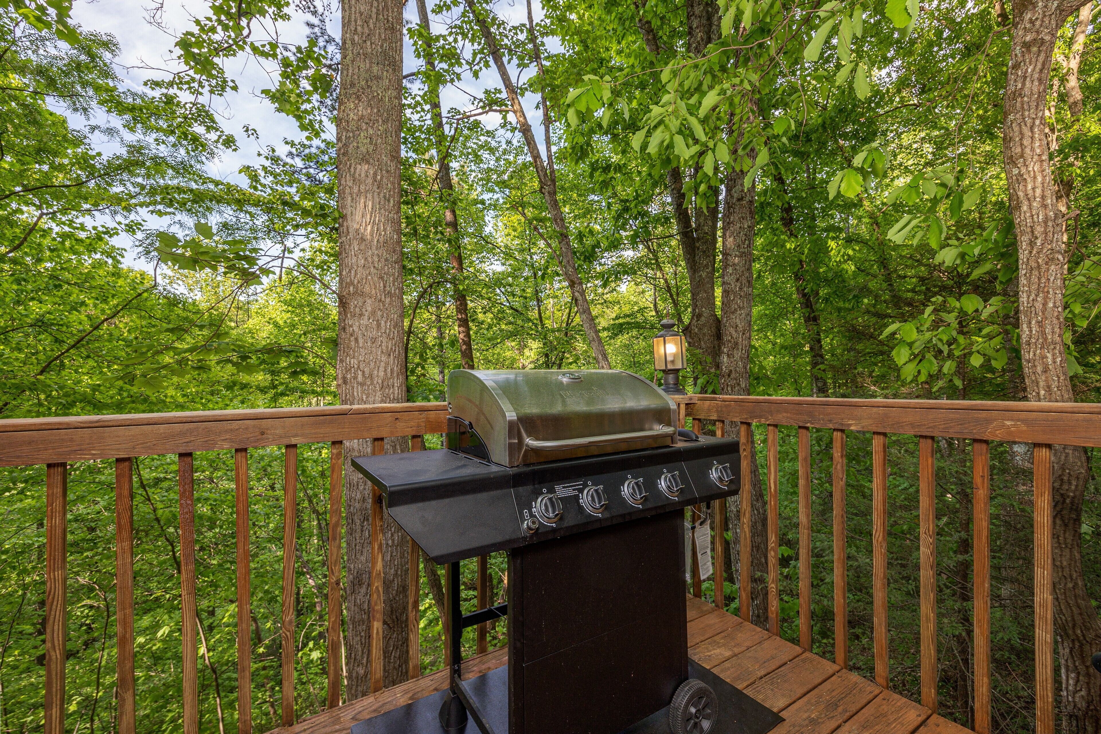 A barbecue grill on a wooden deck surrounded by trees.