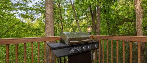 A barbecue grill on a wooden deck surrounded by trees.