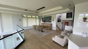 A spacious living area with a wooden dining table, a sofa, and a glass railing overlooking a balcony. - Spacious Tropical Oasis (Princeville)
