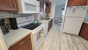 A kitchen with wooden cabinets, a white microwave, a stove, a coffee maker, and a refrigerator. - **NEW FLOORS** BEACH HOUSE, CENTRAL AIR, GOLF CART INCLUDED (Myrtle Beach)