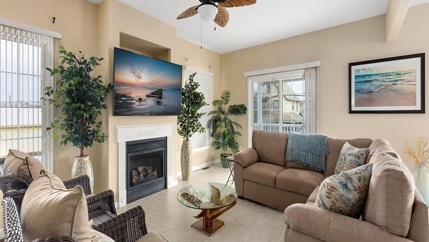 Una sala de estar con chimenea, ventilador de techo y dos grandes ventanas.