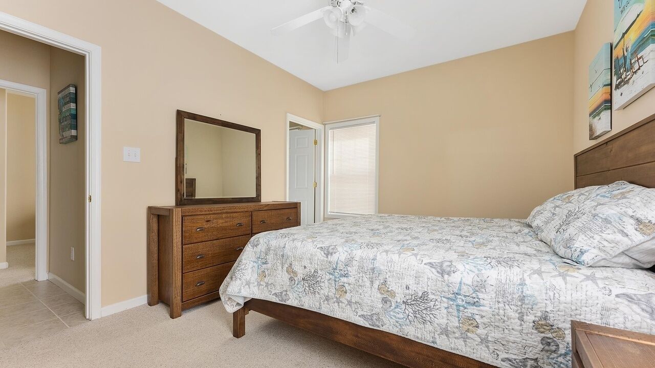 Une chambre à coucher avec un lit, une commode, un miroir et un ventilateur de plafond.