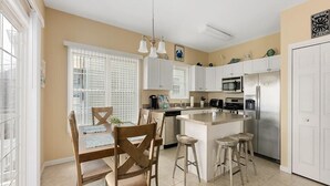 Una cocina con armarios blancos, una isla central con taburetes, un microondas y un refrigerador.