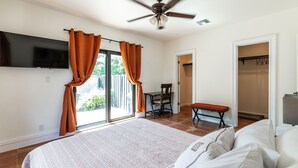 Un dormitorio con una cama grande, un ventilador de techo, un televisor montado en la pared y un ventanal corredero que da a un balcón.