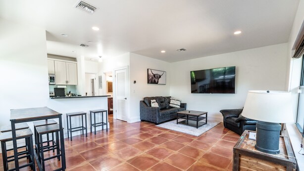 Amplia sala de estar con cocina, sofá gris, mesa de centro y televisor montado en la pared.