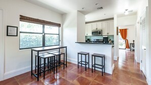 Una cocina moderna con armarios blancos, una isla central y un ventanal con persianas.