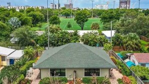 Una casa residencial con techo verde, rodeada de abundante vegetación y un patio cercado.