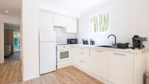 A modern kitchen with white cabinetry, a built-in oven, a microwave, a coffee maker, and a window providing natural light. - 2-Bedroom Apartment with Garden (Cannes)
