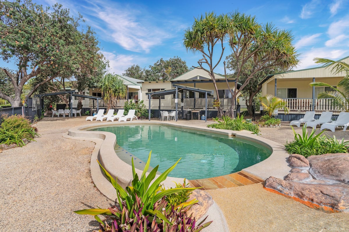 A pool area with lounge chairs, a pool, and a building with multiple balconies.