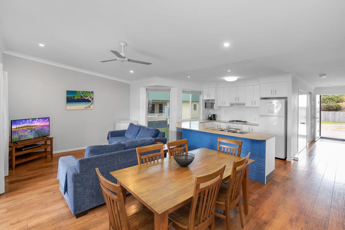 A modern kitchen with white cabinets, a central island, and a dining area with wooden chairs and a table.