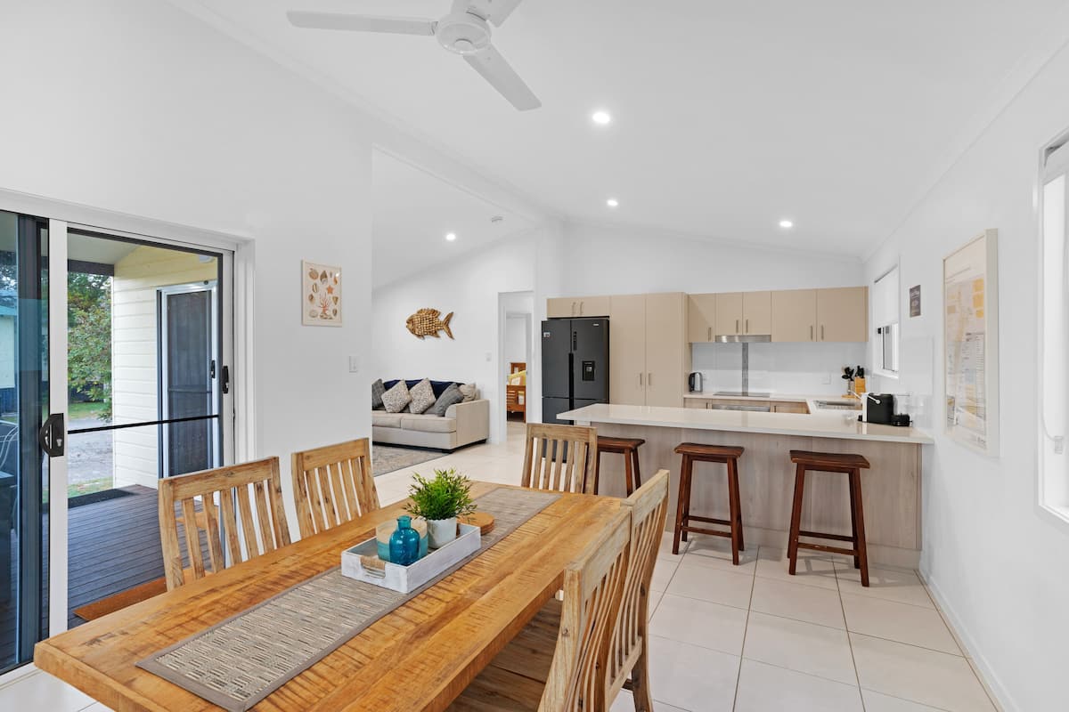 A modern kitchen with a central island, wooden dining table, and bar stools.