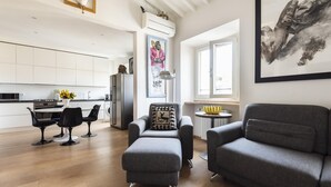 A modern living room with a grey sofa, a grey armchair, and a dining area with black chairs. There is a painting on the wall and a window providing natural light. - Matteotti Apartment in Firenze (Florence)