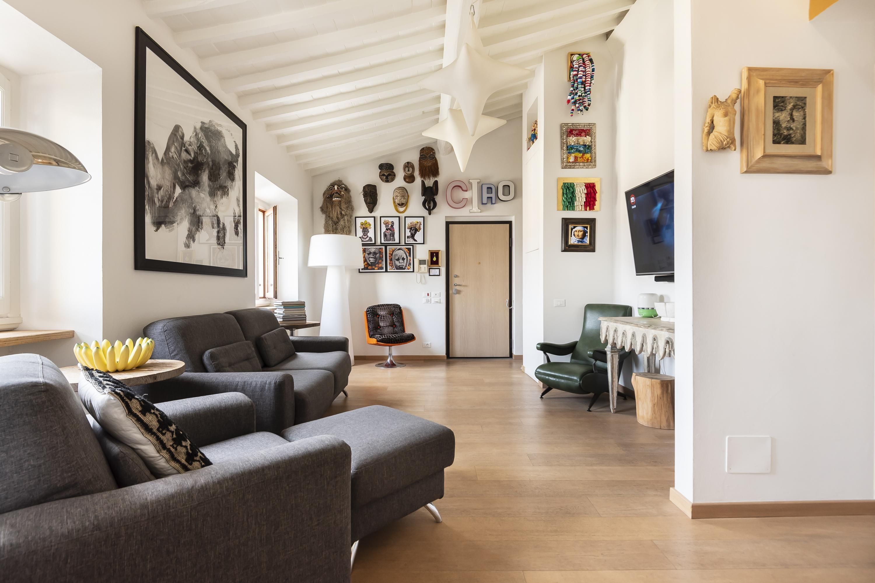 Ein modernes Wohnzimmer mit grauen Sofas, einem großen abstrakten Gemälde und verschiedenen Wanddekorationen, darunter Masken und gerahmte Bilder.