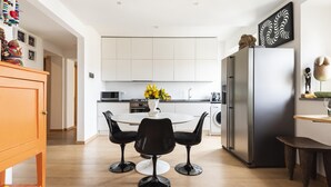 A modern kitchen with white cabinets, a stainless steel refrigerator, and a dining area with black chairs and a white table. - Matteotti Apartment in Firenze (Florence)