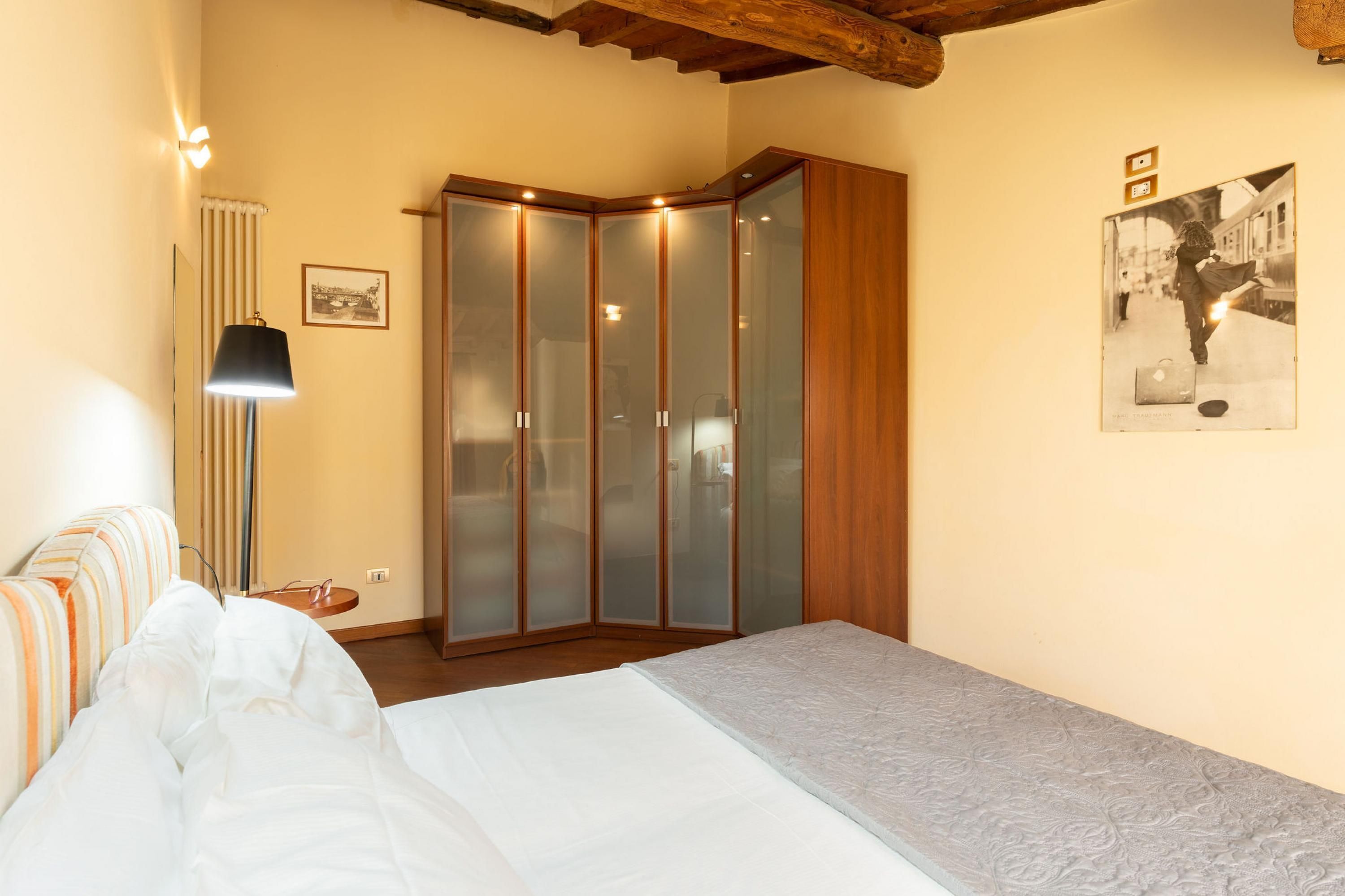 Un dormitorio con cama, armario, lámpara y un cuadro en la pared.