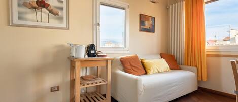 A cozy room with a bed, a small wooden table with a kettle, and a window with curtains.