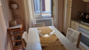 Une petite cuisine avec une table à manger, un radiateur et une fenêtre avec des volets.