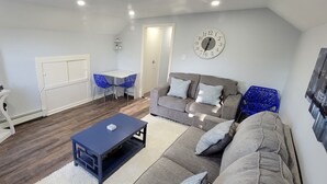 Ein Wohnzimmer mit einem Flachbildfernseher, einem blauen Couchtisch, einem grauen Sofa und einem weißen Schrank.