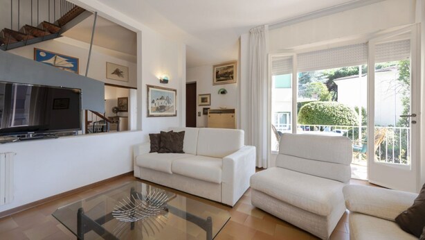 Una sala de estar con sofá, sillón, mesa de vidrio y televisor.
