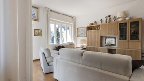Una sala de estar con un sofá, sillones, un aparador con objetos decorativos y un televisor.