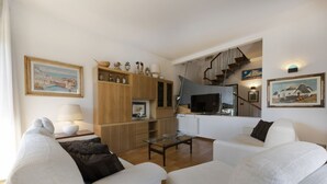 Una sala de estar con sofá, una mesa de centro, televisor y una escalera que sube a un nivel superior.