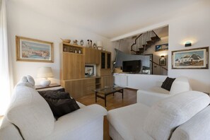 A living room with a sofa, a coffee table, a TV, and a staircase leading to an upper level.