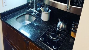 A kitchen with wooden cabinets, a stainless steel microwave, a gas stove, a sink, and a coffee maker. - Spruce Peak, Studio -Ski in -Ski out (Stowe)