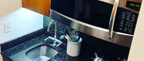Una cocina con armarios de madera, un microondas de acero inoxidable, una estufa a gas, un fregadero y una cafetera.