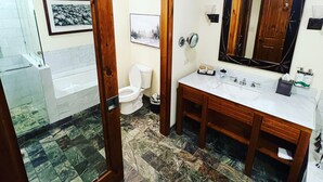 A bathroom with a wooden door, a white toilet, a sink with a mirror, and a shower area. - Spruce Peak, Studio -Ski in -Ski out (Stowe)