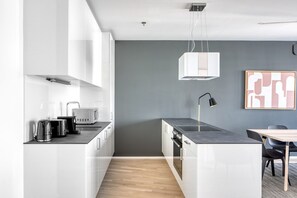Cozinha moderna com armários brancos, bancada preta e piso de madeira.