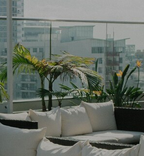 A balcony with a sofa and cushions, surrounded by potted plants and a view of buildings. - Chic Favoriten 1BR w/ Roof, Gym & Lounge, 1min to HBF, by Blueground (Vienna)