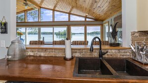 A kitchen with a large window overlooking a lake, a wooden ceiling, and a stone wall. - A Point to Happiness by Lake Martin Vibe (Dadeville)