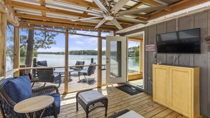 A covered deck with wicker furniture, a television, and a view of a lake. - A Point to Happiness by Lake Martin Vibe (Dadeville)