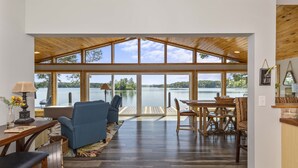 A spacious room with a large window overlooking a lake, furnished with a sofa, chairs, and a dining table. - A Point to Happiness by Lake Martin Vibe (Dadeville)
