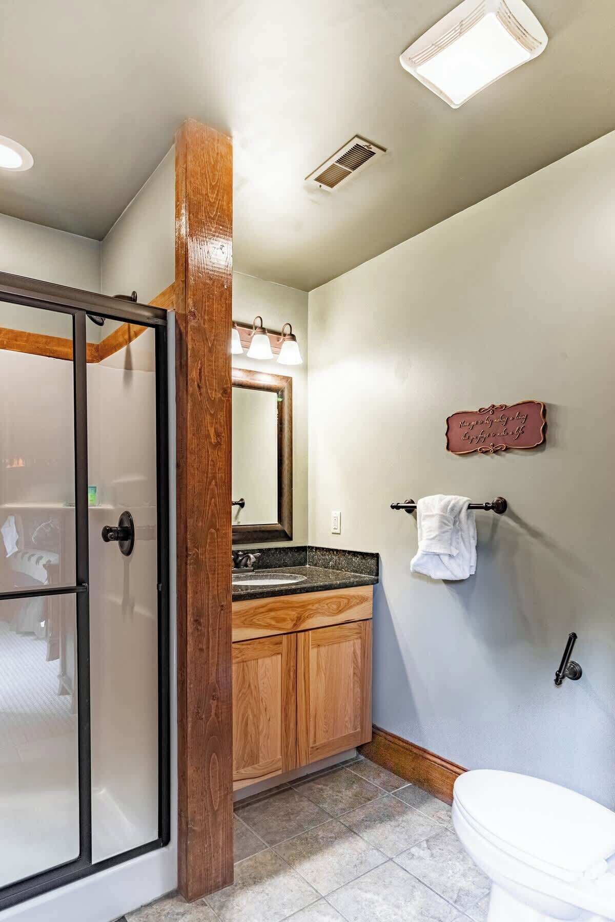 A bathroom with a glass shower door, wooden vanity, a toilet, and a towel rack.