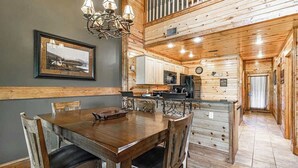 A wooden interior with a dining table, chairs, a chandelier, and a kitchen area. - Cozy Retreat N Smoky, Sleeps 6・Hot Tub・Pool Table (Pigeon Forge)