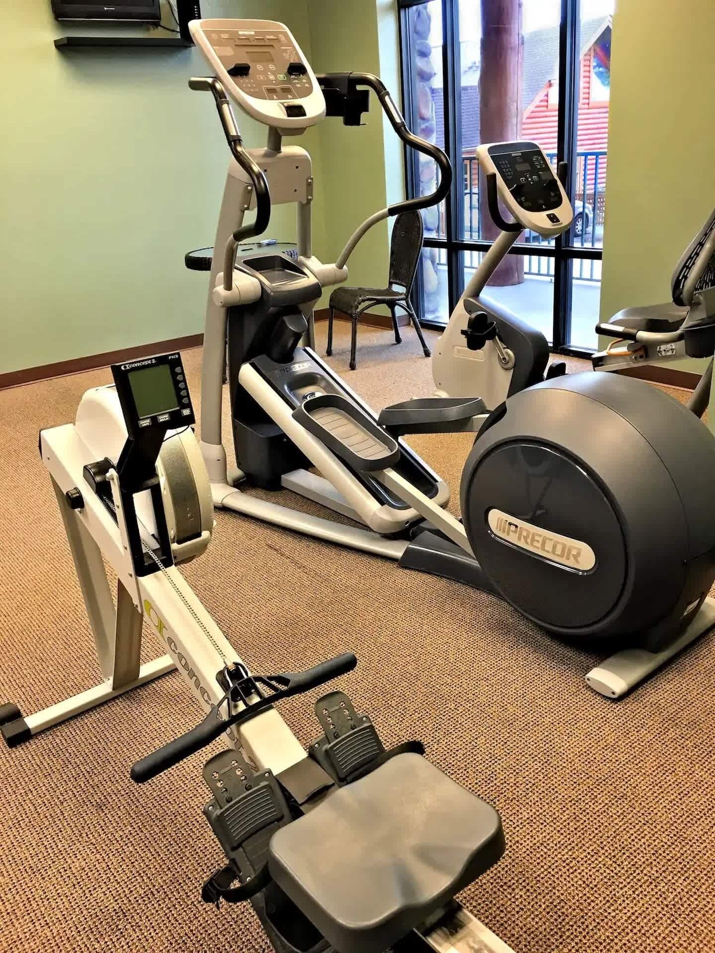 Une salle de sport équipée d’appareils de cardio, notamment un vélo elliptique et un vélo d’appartement, ainsi qu’un grand ballon de gymnastique.