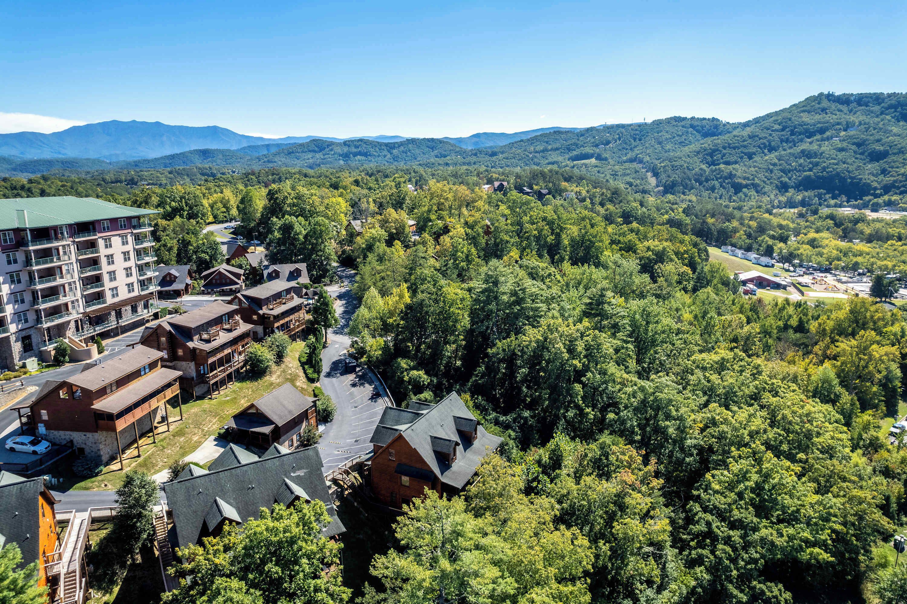 Un complexe hôtelier comprenant plusieurs bâtiments, un parking et offrant une vue sur la forêt et les montagnes environnantes.