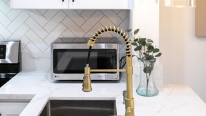 A kitchen with white cabinets, a stainless steel sink, a gold faucet, and a modern light fixture.