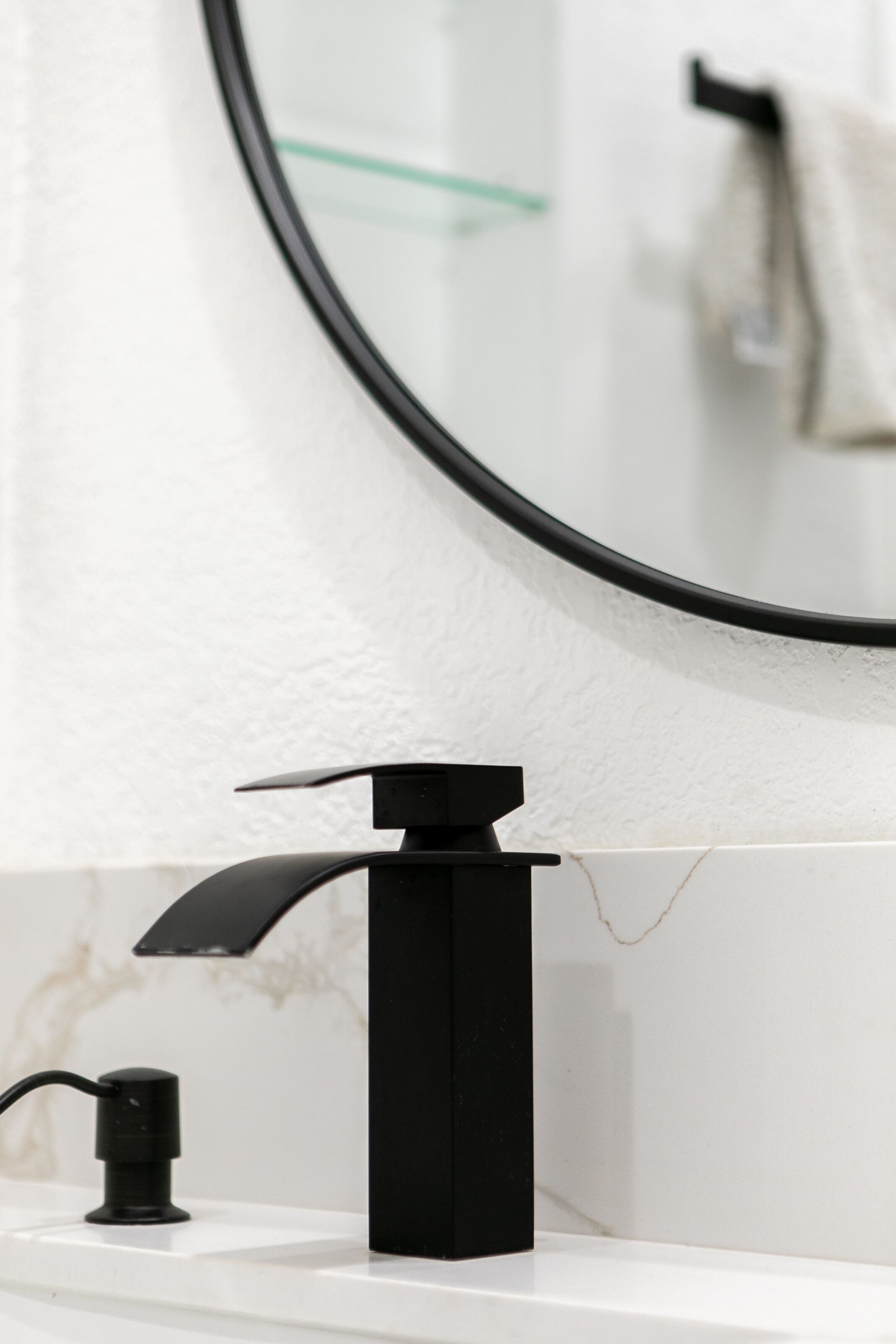 A modern bathroom with a black faucet, a white countertop, and a round mirror.