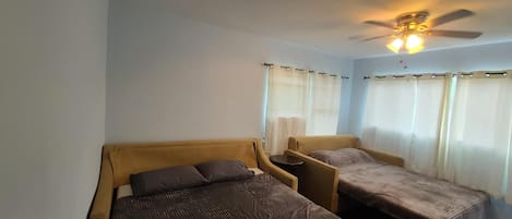 Une chambre avec deux lits, un ventilateur de plafond et des rideaux.
