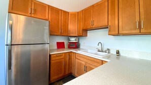 A kitchen with wooden cabinets, a stainless steel refrigerator, a red toaster, and a sink. - Spacious North Shore cottage with lush mountain scenery in the country! (Waialua)